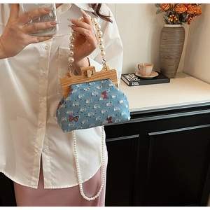 Detail of denim shell bag featuring pearl handle, wood frame and butterfly embroidery