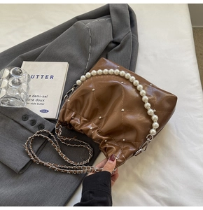 Detail of brown quilted bucket bag with pearl handle and metal rivet accents
