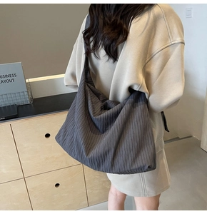 Große dunkelgraue Cord-Hobo-Tasche als Schultertasche an einem Model in beigem Hoodie