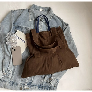 Detail of dark brown canvas tote bag with contrast blue denim handles and large capacity