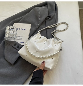 Detail of white quilted bucket bag with pearl handle and silver studs on grey blazer