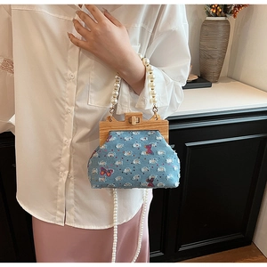 Detail of denim bag featuring colorful butterfly embroidery and wood frame closure