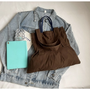 Close-up of deep brown canvas tote bag with vertical stitching on blue denim jacket