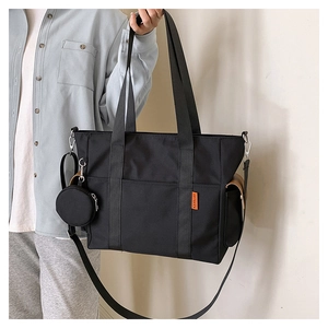 Detail of black nylon tote bag showing orange label, side pocket, and small round pouch