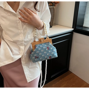 Detail of blue denim seashell bag with pearl handle and red bow sequin accents