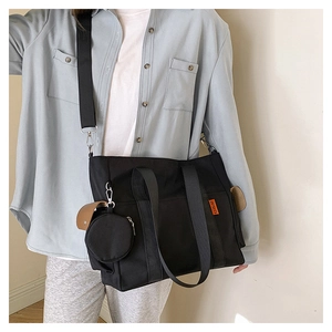 Detail view of black canvas tote bag with round coin purse and brown leather buckle strap