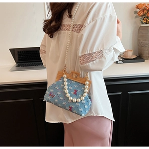 Detailed view of denim shell bag with sequined butterflies and white pearl handle strap