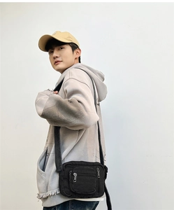 Detail view of mini black canvas crossbody bag with multiple zip pockets on model