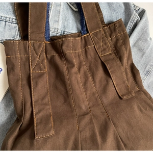 Detail of a brown canvas tote bag featuring reinforced X-shaped stitching and denim handles