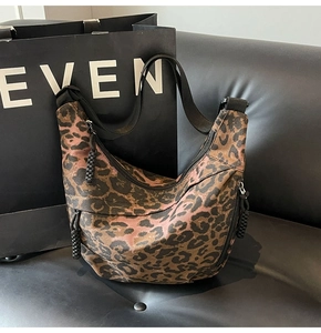 Close-up of leopard print canvas crescent bag with black strap on leather background
