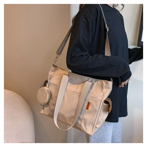 Detail of beige nylon tote bag with side pockets and a round coin purse charm