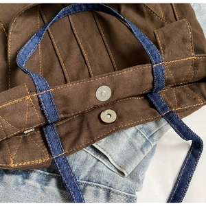 Detail of the magnetic metal buckle and navy denim handles on the brown canvas tote bag