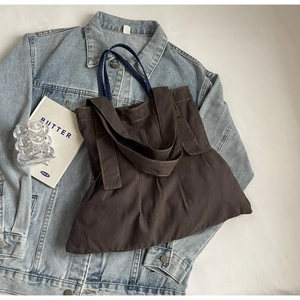 Deep brown canvas tote bag with pleated texture laid on denim jacket for retro style