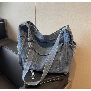 Detailed view of dark blue denim tote bag with frayed edges and adjustable strap on a chair