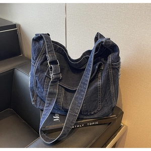 Detail view of dark blue denim hobo bag featuring frayed edges and adjustable silver buckle