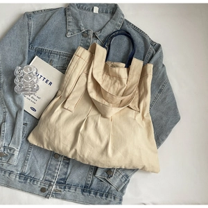 Detail of beige canvas tote bag with vertical pleats and blue braided rope handles