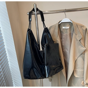 Black large capacity tote bag set hanging next to a trench coat in a minimalist setting