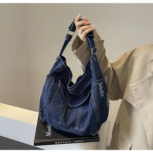 Detail of dark blue denim hobo bag featuring frayed edges and adjustable buckle strap