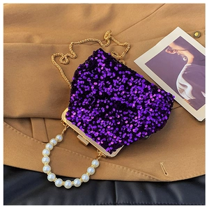 Detail der lila Pailletten-Muscheltasche mit Goldkette und weißem Perlengriff auf Stoff