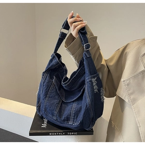 Detail of dark blue denim hobo bag featuring distressed fringe and silver metal buckle