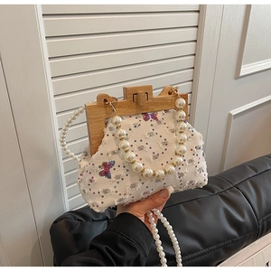 Detailed view of beaded pearl handle and butterfly embroidery on a white tweed handbag