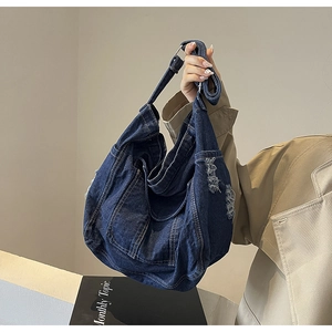 Detail of distressed denim tote bag with frayed edges and adjustable shoulder strap
