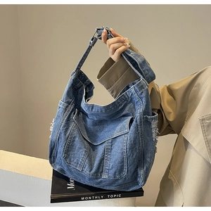 Detailed view of frayed edges and functional flap pockets on blue denim tote bag