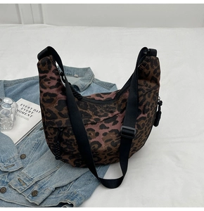 Detail of leopard print canvas crescent bag featuring adjustable black strap and zipper