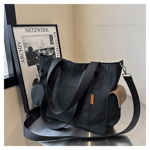 Detail of black canvas tote bag showing side pocket, brown leather trim, and round coin purse
