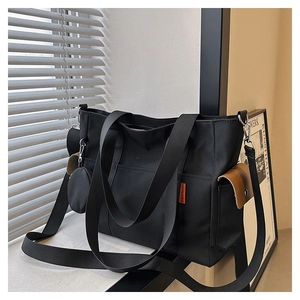 Detail view of black canvas tote bag with side pocket and brown leather flip detail