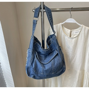 Detailed close-up of dark blue denim tote bag with multi-pocket and silver buckle strap
