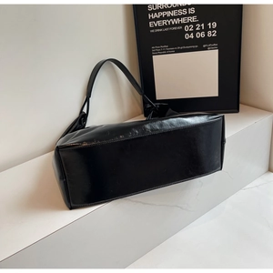 Detail of a minimalist black polished leather tote bag with thin straps on a white stand