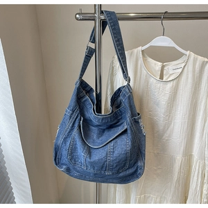 Detail of blue washed denim tote bag with frayed edges and adjustable shoulder strap