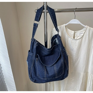 Detail of dark blue denim tote bag featuring distressed edges and front flap pocket