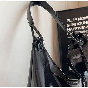 Detail of black glossy hobo bag featuring a knotted shoulder strap and metallic eyelet