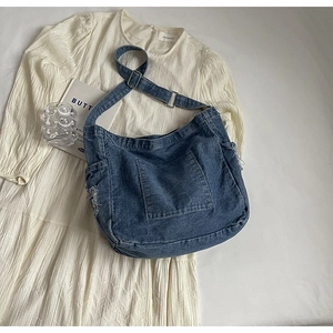 Detail of adjustable metal buckle and distressed frayed edges on dark blue denim tote bag