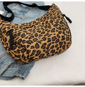 Close-up of leopard print canvas crescent bag with adjustable black strap on white background