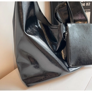 Detail of glossy black shoulder bag featuring textured leather and matching mini pouch
