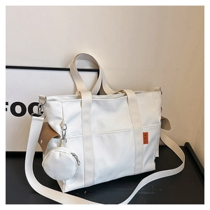 Detail of white canvas tote with orange label, brown leather flap, and small round pouch