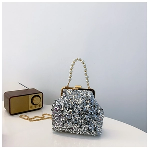 Nahaufnahme einer silbernen Pailletten-Muscheltasche mit Perlengriff und Goldkette