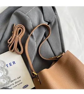 Détail du sac seau en cuir grainé marron avec boucle dorée posé sur un blazer gris chic