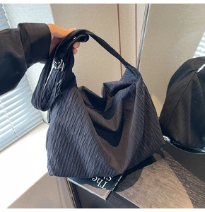 Makroaufnahme der schwarzen Faltenstruktur und Metallschnalle an der Schultertasche