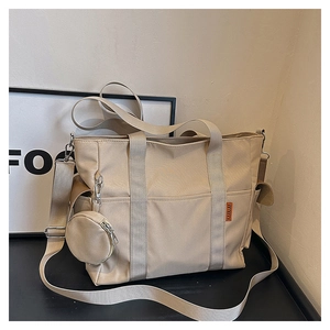 Detail view of the beige canvas tote bag showing the orange logo tag and small coin purse
