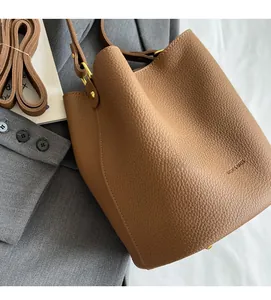 Détail du sac seau en cuir marron avec motif litchi, ferrures dorées et pieds en métal