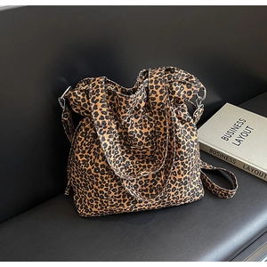 Detail of leopard print canvas tote bag with metal hardware on leather background