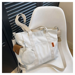 Detail of off-white canvas tote bag with hanging coin purse and brown leather pocket accent