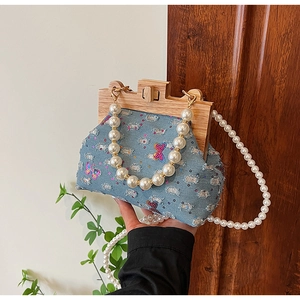 Detail of denim shell bag featuring sequin butterfly embroidery and wooden frame handle