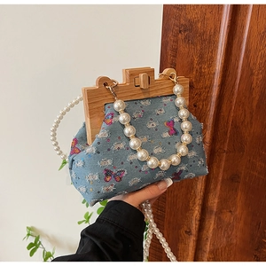 Close-up of denim shell bag with sequined butterflies, wooden frame, and pearl straps