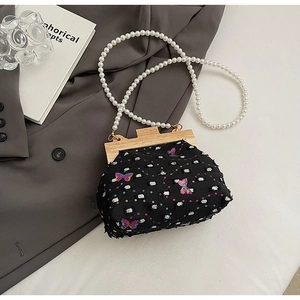 Detail of shell-shaped bag with butterfly embroidery and pearl strap on fabric
