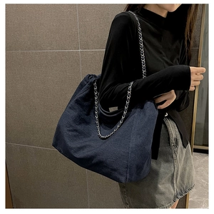 Detail of blue denim tote bag featuring silver metal chain strap and pleated closure